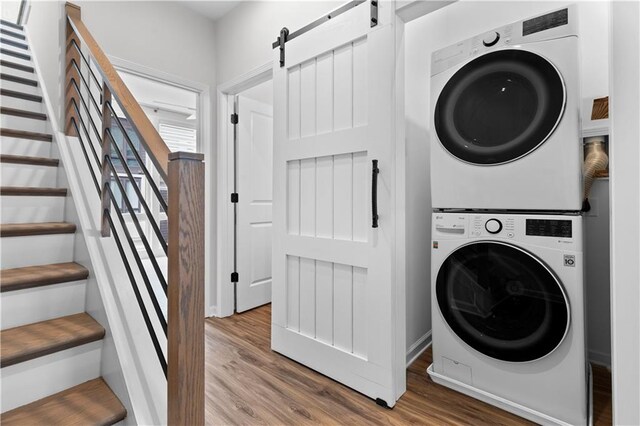 laundry area with a barn door, stacked washer and dryer, and hardwood / wood-style floors