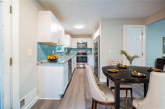 10150 Puckett St, Covington, GA 30014 - kitchen featuring appliances with stainless steel finishes, light wood-style floors, white cabinets, and tasteful backsplash