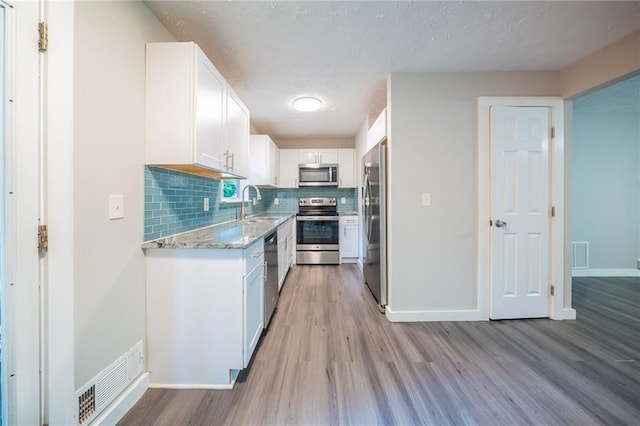 10150 Puckett St, Covington, GA 30014 - kitchen featuring stainless steel appliances, light wood-style flooring, white cabinets, decorative backsplash, and a textured ceiling