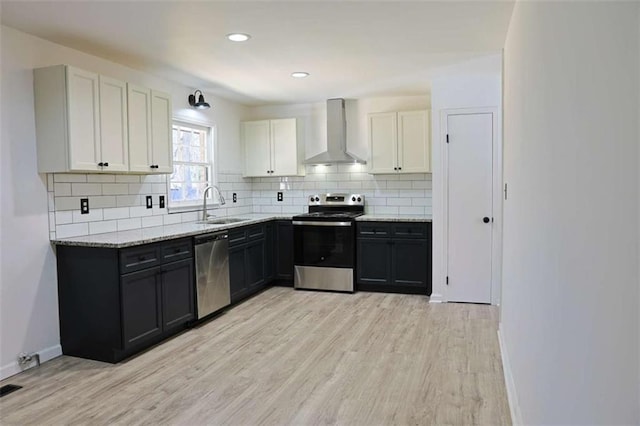 kitchen featuring light wood-style flooring, a sink, appliances with stainless steel finishes, wall chimney range hood, and decorative backsplash