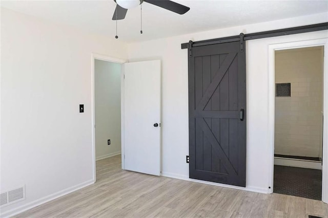 unfurnished bedroom with light wood-style floors, a barn door, visible vents, and baseboards