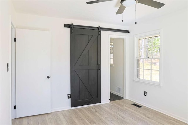 interior space featuring a barn door, wood finished floors, visible vents, and baseboards