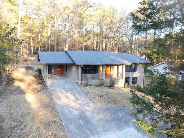 ranch-style home with covered porch, concrete driveway, an attached carport, and a shingled roof