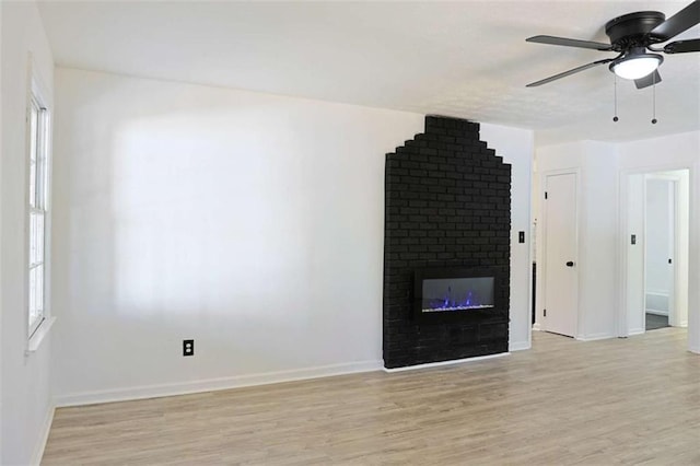 unfurnished living room featuring baseboards, a fireplace, a ceiling fan, and light wood-style floors