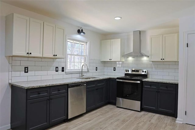 kitchen with light wood-style flooring, decorative backsplash, appliances with stainless steel finishes, a sink, and wall chimney range hood