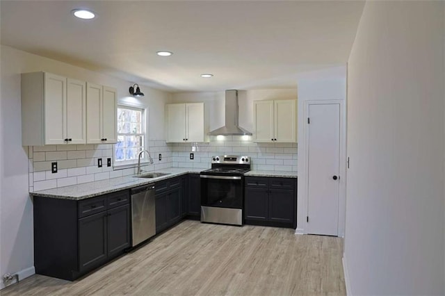 kitchen featuring light wood-style floors, appliances with stainless steel finishes, light stone countertops, wall chimney range hood, and a sink