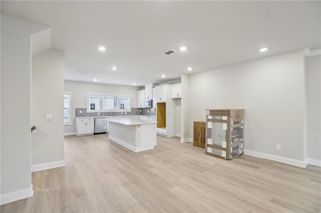 kitchen with a kitchen island, white cabinets, decorative backsplash, stainless steel appliances, and light hardwood / wood-style flooring