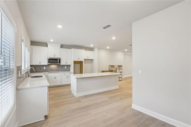 kitchen featuring sink, white cabinetry, a center island, light hardwood / wood-style flooring, and backsplash