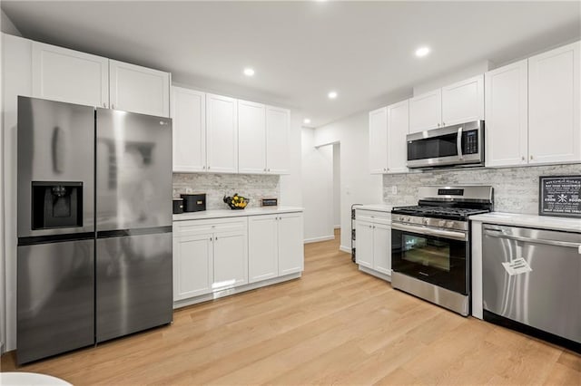 kitchen with white cabinets, appliances with stainless steel finishes, light hardwood / wood-style floors, and decorative backsplash