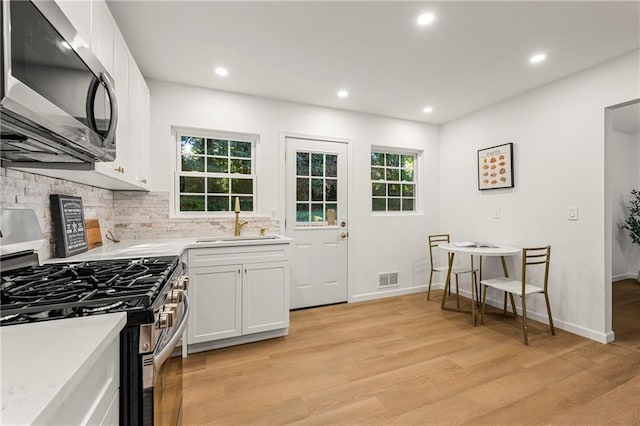 kitchen with white cabinets, sink, light hardwood / wood-style flooring, appliances with stainless steel finishes, and tasteful backsplash