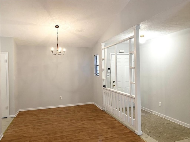 unfurnished room with hardwood / wood-style floors, vaulted ceiling, and an inviting chandelier