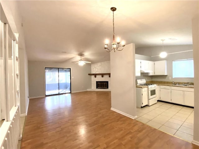 kitchen with gas range gas stove, hanging light fixtures, a stone fireplace, lofted ceiling, and white cabinets