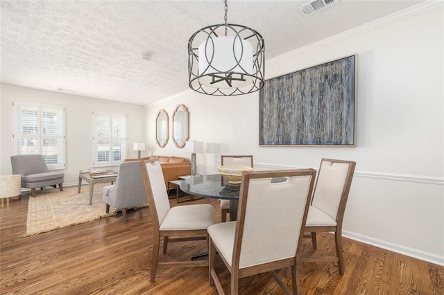 dining room featuring dark hardwood / wood-style flooring, crown molding, a textured ceiling, and a notable chandelier