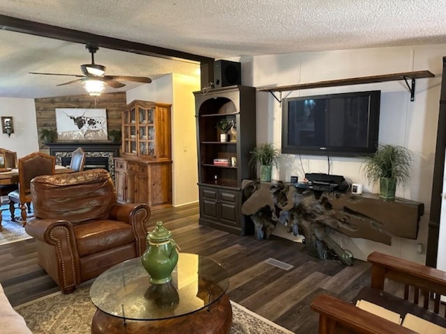 living area with beamed ceiling, a textured ceiling, wood finished floors, a fireplace, and ceiling fan