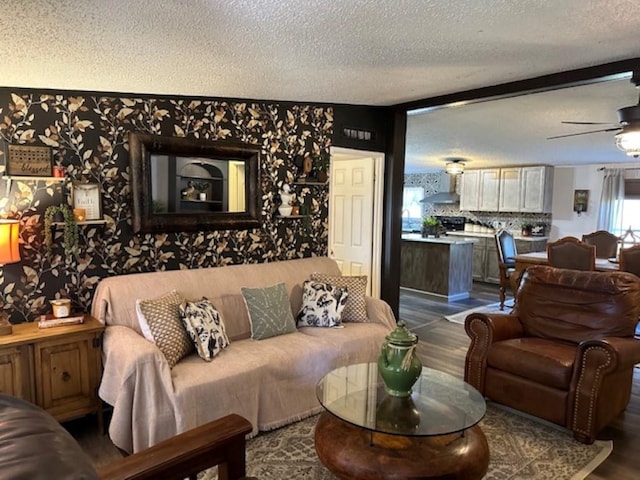 living area featuring ceiling fan, dark wood-style floors, wallpapered walls, and a textured ceiling