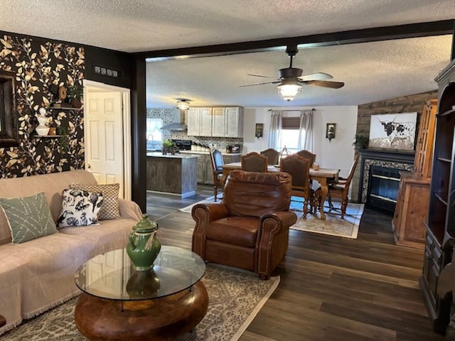 living room featuring dark wood-type flooring, beamed ceiling, a fireplace, a textured ceiling, and a ceiling fan