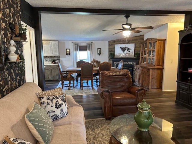 living room featuring beam ceiling, a textured ceiling, wood finished floors, a fireplace, and ceiling fan