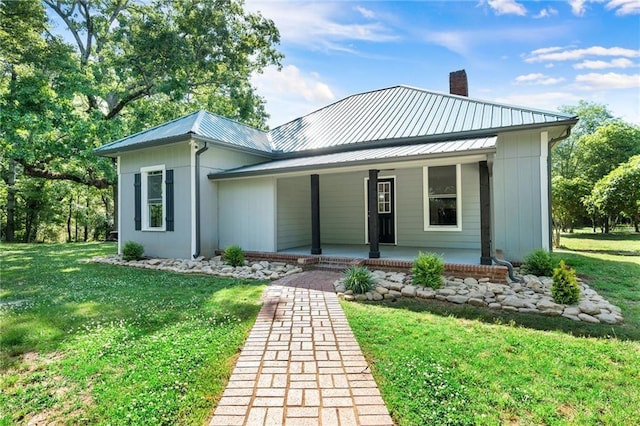 view of front facade featuring covered porch, a chimney, metal roof, and a front yard