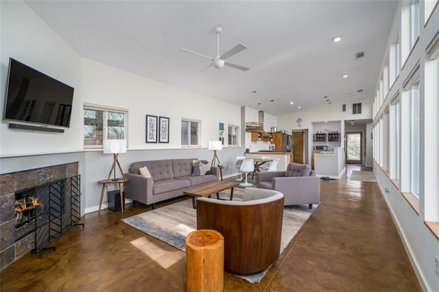 living area featuring finished concrete flooring, a ceiling fan, a tiled fireplace, visible vents, and baseboards