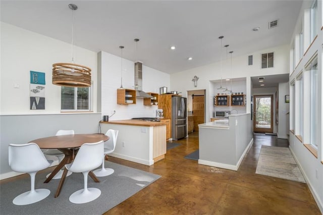 kitchen with visible vents, a peninsula, appliances with stainless steel finishes, and wall chimney exhaust hood