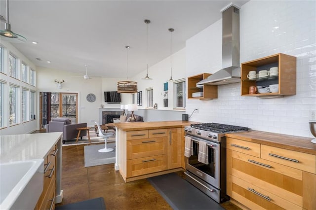 kitchen featuring stainless steel range with gas cooktop, butcher block countertops, wall chimney range hood, a fireplace, and decorative backsplash