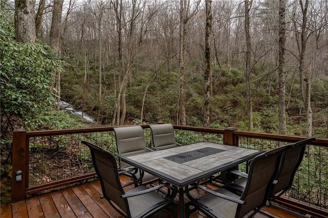 wooden terrace featuring a wooded view and outdoor dining space