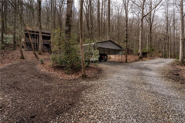 view of front of home with gravel driveway, a carport, and a view of trees