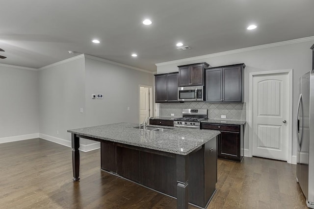 kitchen featuring dark wood-type flooring, a sink, appliances with stainless steel finishes, decorative backsplash, and a center island with sink