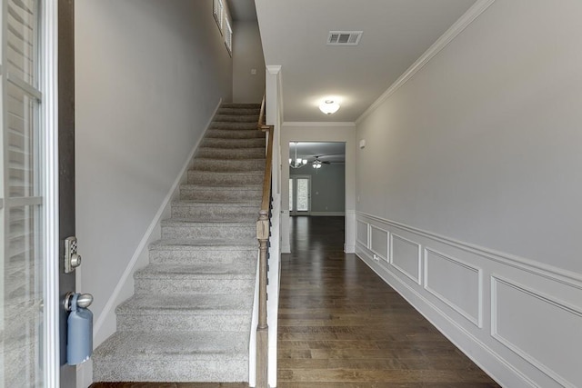 staircase with a wainscoted wall, visible vents, a decorative wall, ornamental molding, and wood finished floors