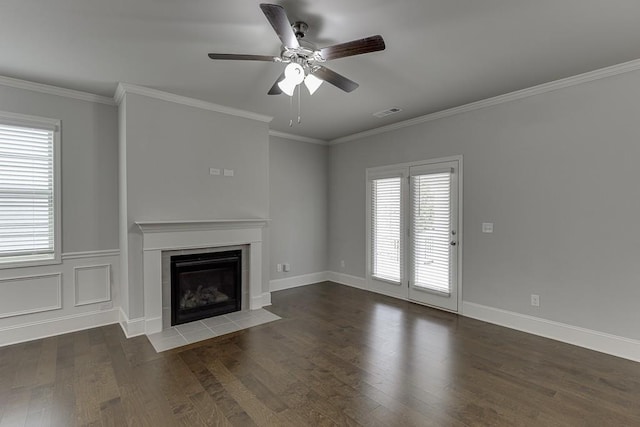 unfurnished living room with visible vents, a tiled fireplace, ornamental molding, a ceiling fan, and wood finished floors