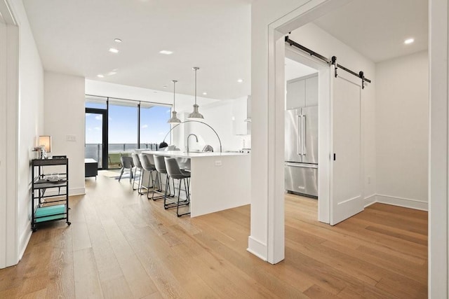 interior space featuring pendant lighting, a kitchen breakfast bar, light wood-type flooring, high end refrigerator, and a barn door