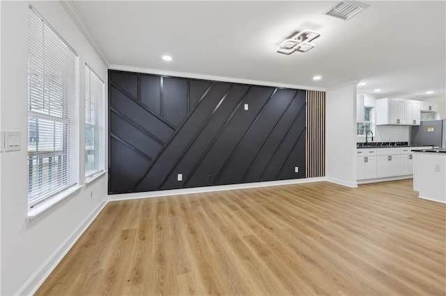 empty room with crown molding, sink, and light hardwood / wood-style floors