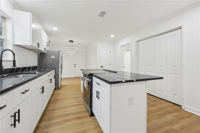 kitchen with sink, appliances with stainless steel finishes, white cabinets, a kitchen island, and light wood-type flooring