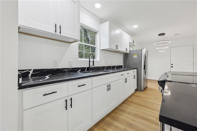 kitchen featuring stainless steel refrigerator with ice dispenser, sink, dark stone countertops, pendant lighting, and white cabinets