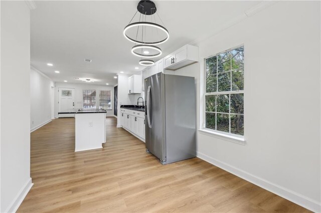 kitchen featuring white cabinetry, crown molding, decorative light fixtures, light hardwood / wood-style flooring, and stainless steel fridge