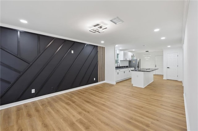 kitchen featuring stainless steel fridge, a kitchen island with sink, white cabinets, and light wood-type flooring