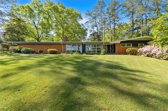 rear view of property with a chimney, a lawn, and brick siding