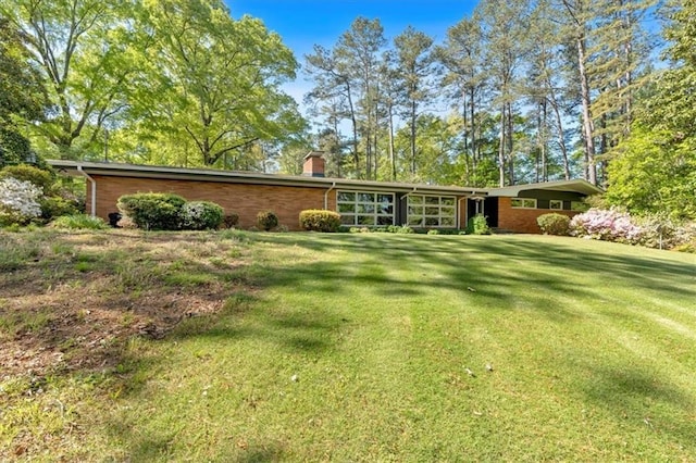 rear view of property featuring a chimney, a lawn, and brick siding