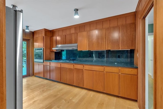 kitchen featuring under cabinet range hood, stainless steel appliances, decorative backsplash, and dark countertops