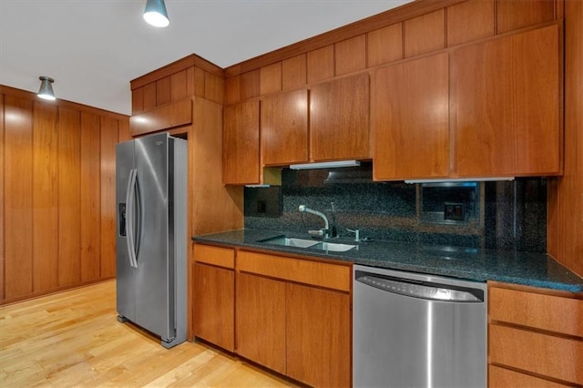 kitchen with appliances with stainless steel finishes, a sink, decorative backsplash, light wood finished floors, and brown cabinetry