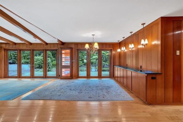 unfurnished dining area featuring plenty of natural light, wood walls, a chandelier, light wood-style flooring, and beamed ceiling