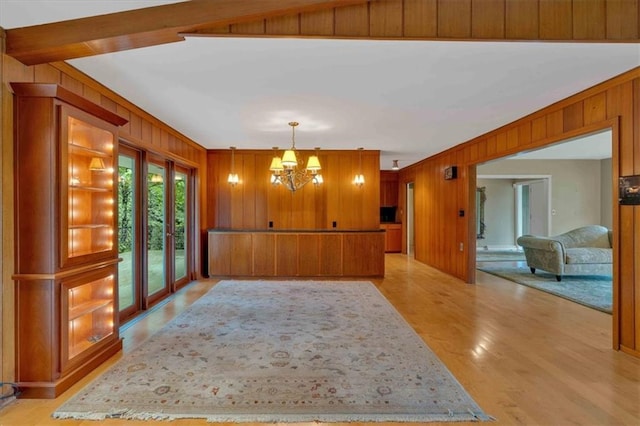 unfurnished dining area with wooden walls, a chandelier, and light wood-type flooring