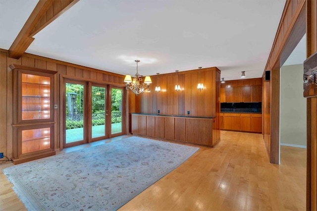 unfurnished dining area with a chandelier, wood walls, light wood finished floors, and baseboards