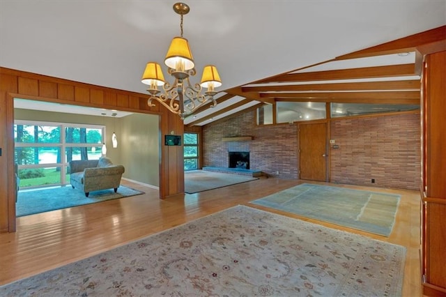 unfurnished living room with wood finished floors, a chandelier, brick wall, and a large fireplace