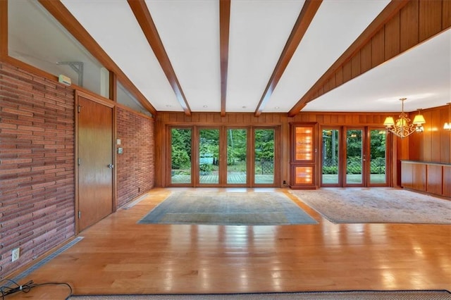 unfurnished living room with a chandelier, brick wall, wood walls, and wood finished floors