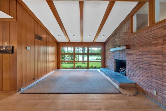 unfurnished living room with wood finished floors, a brick fireplace, brick wall, and wooden walls