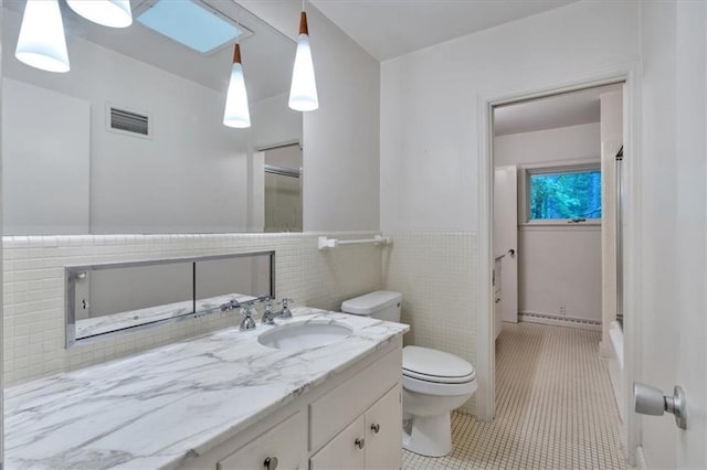 bathroom featuring tile patterned floors, toilet, vanity, wainscoting, and a shower