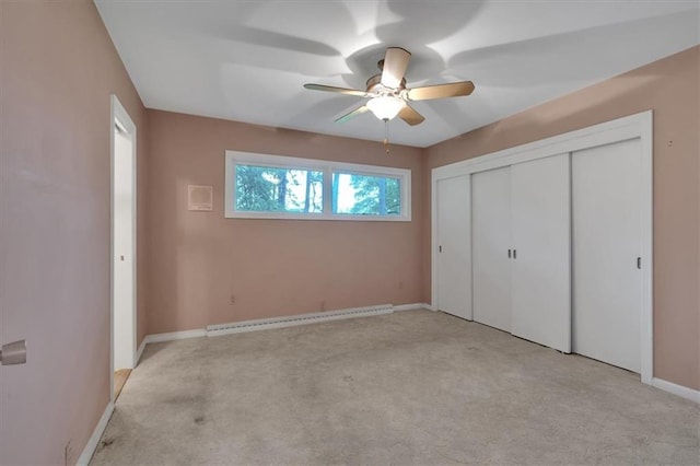 unfurnished bedroom featuring light colored carpet, a baseboard heating unit, baseboards, a closet, and a ceiling fan