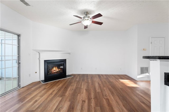 unfurnished living room featuring a glass covered fireplace, visible vents, a textured ceiling, and wood finished floors