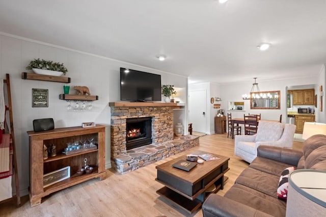 living room featuring crown molding, a chandelier, wood finished floors, and a stone fireplace